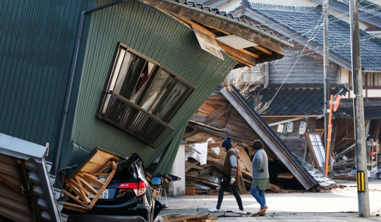 Residents walk past a damaged house, following an earthquake, in Nanao, Ishikawa prefecture, Japan, on January 2, 2024